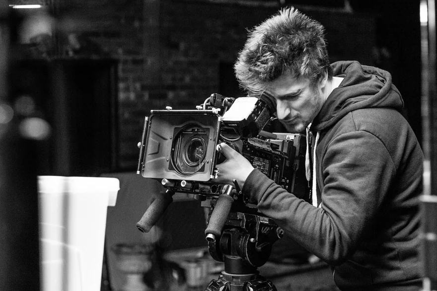 Black-and-white close-up of a camera operator looking through a cinema camera viewfinder